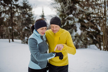 Senior couple looking at smartwatch during winter jogging.