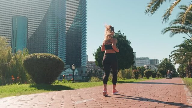 Manager does morning run before start of working day. Woman in black tracksuit runs on treadmill against backdrop of giant modern buildings of city.