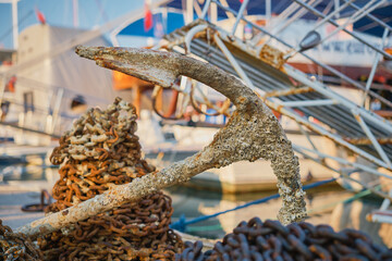 View of the old rusty anchor with a chain in the port of the city. Anchor of an old ship on the pier, selective focus, background or screen about holidays at sea and travel