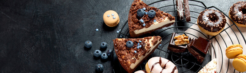 Table with various cookies, donuts, cakes, cheesecakes on dark background.