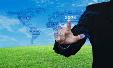 Businessman pressing 2023 start up business icon with global words world map over green grass with...
