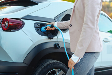 Close-up of woman holding power supply cable from her electric car, charging it in home,...
