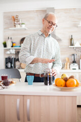 Senior man making coffee using french press during breakfast in kitchen. Elderly person in the...