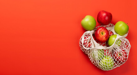 Red and green apples in mesh bag on red