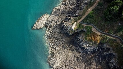 Aerial shot of rocky edge of an island in the ocean with a narrow road on it - Powered by Adobe