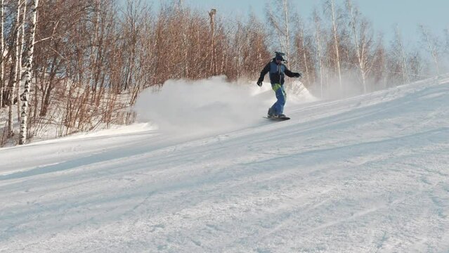 A snowboarder rides from a hill, makes several tricks and falls at high speed on a sunny winter day at the ski resort. Snowboard buttering tricks.