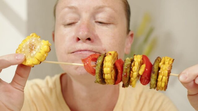 Vegan woman eating grilled vegetables from skewer. 
