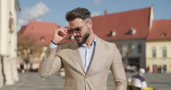 cool elegant man with beard adjusting glasses and suit, looking to side and being confident outside in a medieval town