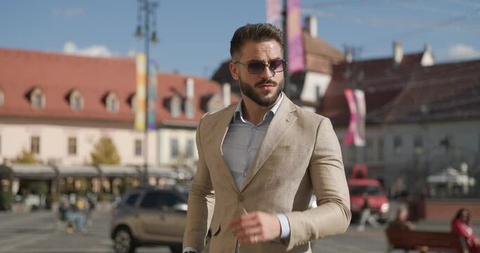 sexy Latin guy looking to side, arranging suit and glasses, being cool and confident while looking around and admiring the city