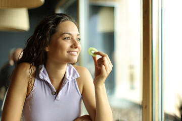 Happy woman in a restaurant eating kiwi looking away