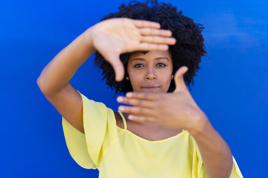 Happy young woman making frame with hands in front of blue background