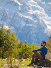 journey by Irkis valley, Arkhyz, Karachay-Cherkessia, North Caucasus. Man hiking up mountain in snowy mountain valley with blue sky and clouds and beautiful forest near river Psysh, Caucasus.