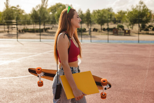 Woman walking with file and skateboard in sports court