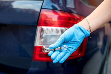 Close-up of a mechanic in rubber gloves holding a halogen lamp in his hand.