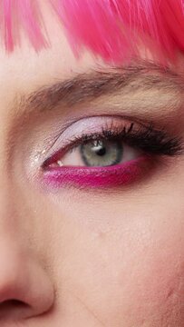 Vertical video: Macro shot of positive woman with glamour colorful eye makeup and pink hair posing in studio, having fun and feeling confident. Healthy positive beauty model with big eyelashes