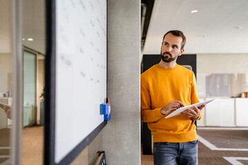 Determined businessman with tablet PC looking at white board in office