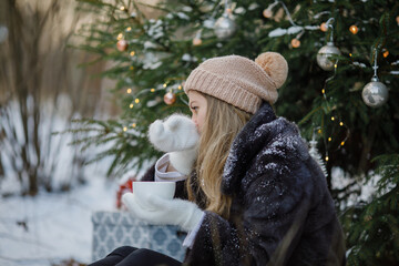 a middle-aged woman under a Christmas tree in the forest before Christmas holds a cup of mulled wine in her hands