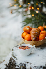 a cup of hot mulled wine with orange and cinnamon and a dish of oranges and croissants in the forest under a Christmas tree decorated