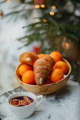 a cup of hot mulled wine with orange and cinnamon and a dish of oranges and croissants in the forest under a Christmas tree decorated