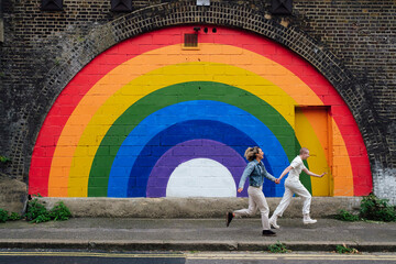 Carefree woman with non binary friend holding hands running on footpath