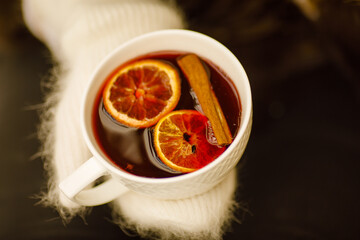 close-up female hands holding a cup of hot mulled wine with orange and cinnamon