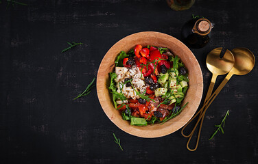 Fresh salad with avocado, tomatoes, mozzarella cheese, sweet peppers and black olives on wooden bowl. Top view, above