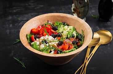 Fresh salad with avocado, tomatoes, mozzarella cheese, sweet peppers and black olives on wooden bowl.