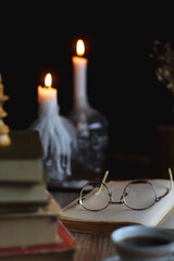 Stack of vintage books, cup of tea or coffee, lit candles, reading glasses and chess pieces on...