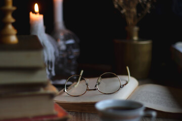 Stack of vintage books, cup of tea or coffee, lit candles, reading glasses and chess pieces on...