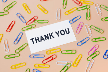 Thank you message on card for presentation, business. Top view of business card and many colourful paper clips on beige background. Flat lay design