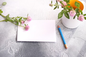 Empty paper sheet with pencil. A sprigs of clover on the table and on the mug. Sweet moments in cozy home
