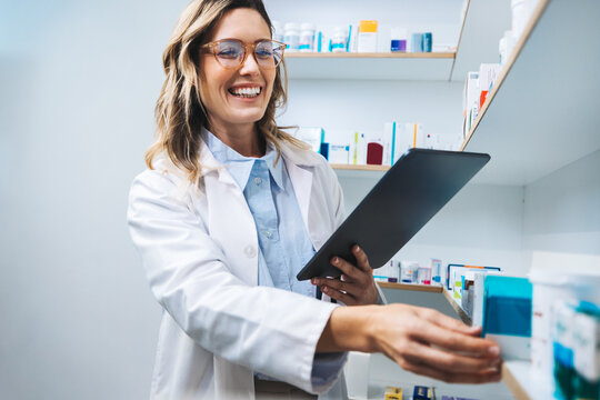 Happy pharmacist getting prescription medication from a shelf in a chemist.