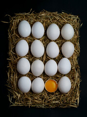 Chicken egg half broken among other eggs lie on a black background
