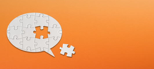 Speech bubble made of white jigsaw puzzle pieces on orange background. A missing piece of the...