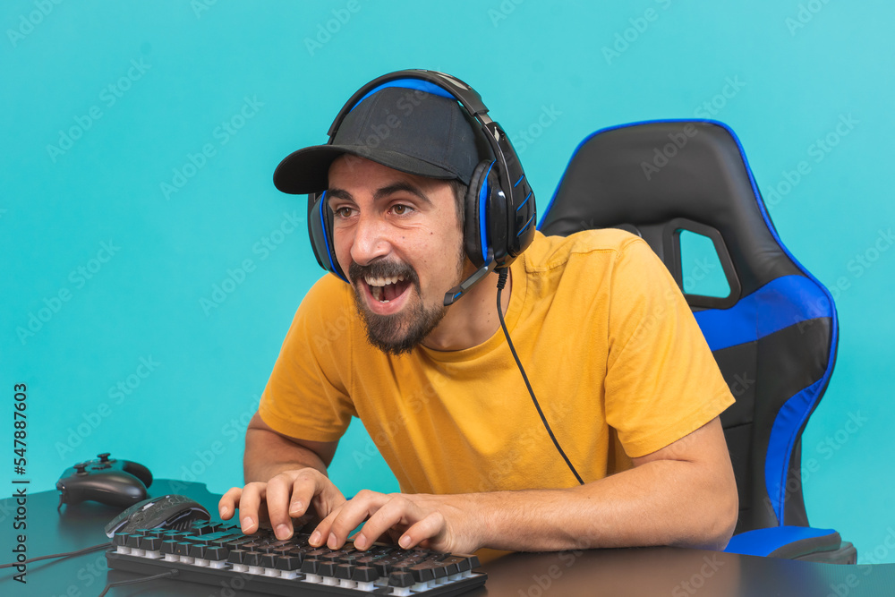 Wall mural excited handsome young male gamer playing online game on computer isolated on blue background. guy w - Wall murals