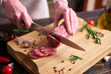 Woman slicing Traditional salami sausage on wooden cutting board by a knife at domestic kitchen