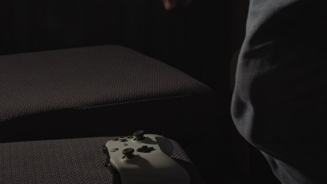 Male Hands playing with a videogame controller and putting it down and man standing up in a dark living room