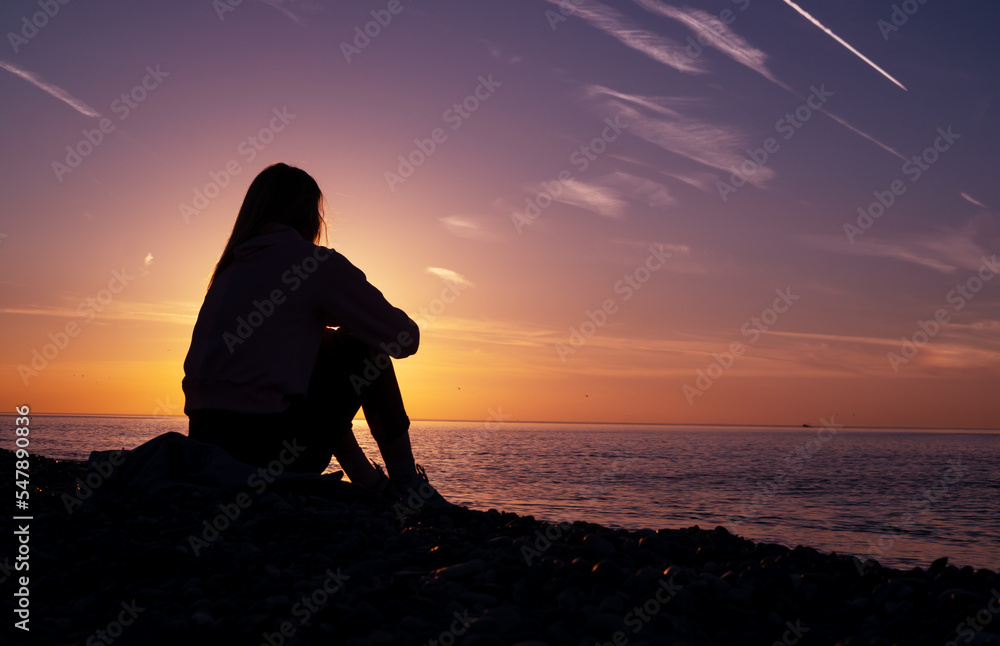 Wall mural a girl is sitting on the beach watching the sunset.