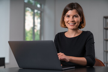 Smiling attractive businesswoman in formal wear typing on laptop