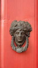 Cast doorknob in the shape of an ancient Roman woman's head on a red door. Antique door knocker