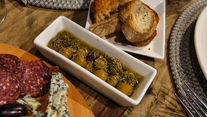 Top view of wine appetizers; cheese, salami,, toast bread and green olives with thyme served in olive oil in a small plate