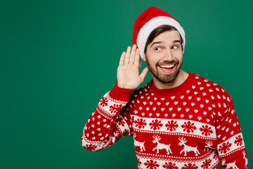 Merry young man 20s wear red warm knitted sweater Santa hat posing try to hear you overhear...