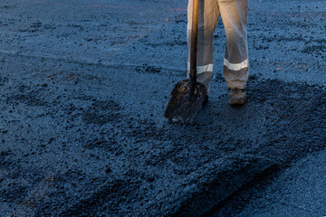 Road construction background. Worker with a shovel standing on fresh paving asphalt during road...