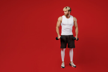 Fototapeta na wymiar Full body young young strong sporty toned sportsman man wearing white clothes spend time in home gym hold dumbbells look aside on area isolated on plain red background Workout sport fit body concept.