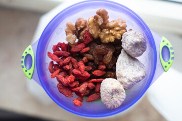 Isolated bright blu plastic cup with dried fruits and nuts. Walnuts, goji, figs and dark raisin mix for breakfast. Raw and healthy food contest. Natural vitamin products. Close up picture.