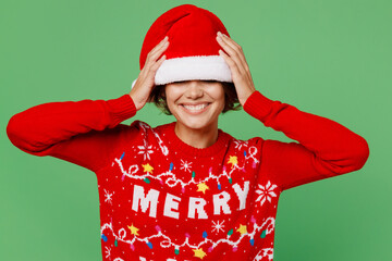 Merry smiling fun cool young woman wear knitted xmas sweater posing cover eyes with Santa hat hold...