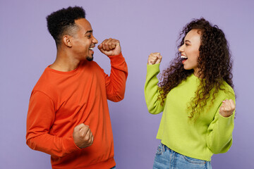 Side view young couple two friend family man woman of African American ethnicity wear casual clothes together do winner gesture celebrate clench fists isolated on pastel plain light purple background
