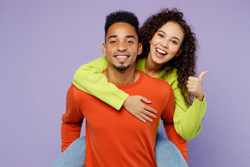 Young couple two friends family man woman of African American ethnicity 20s wear casual clothes together giving piggyback ride to joyful, sit on back show thumb up isolated on plain purple background.