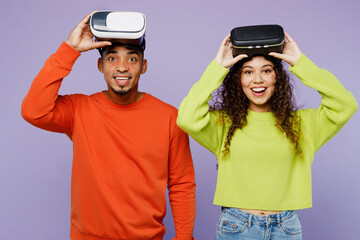 Young excited surprised couple two friend family man woman of African American ethnicity wear casual clothes together watching in vr headset pc gadget isolated on pastel plain light purple background