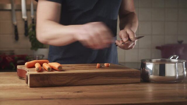 Male home chef chopping carrots on a wooden cutting board. Home cooking concept. Low angle shot.